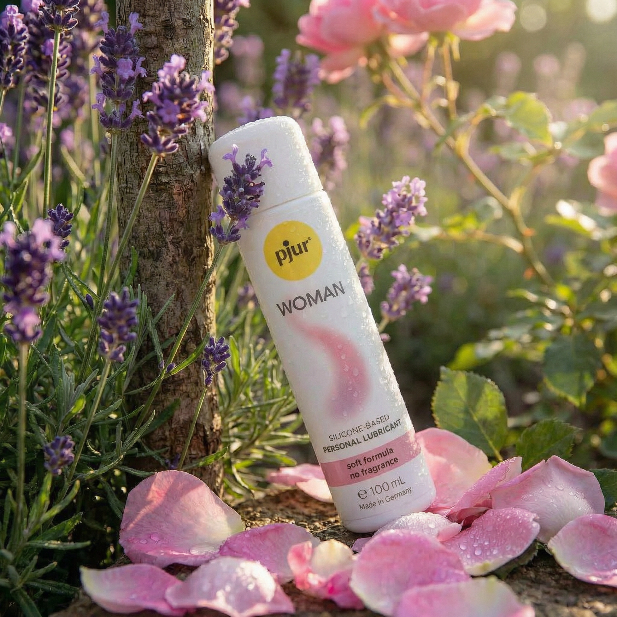 pjur Woman fles met waterdruppels tussen lavendel, roze rozenblaadjes en rozenstruik in zonlicht