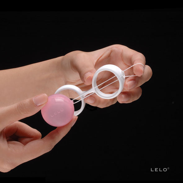 Luna Beads LELO wit siliconen harnas met roze balletje vastgehouden in vrouwenhand tegen zwarte achtergrond