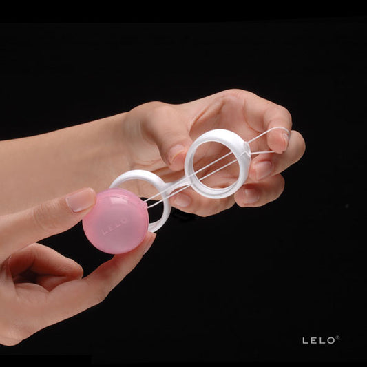 Luna Beads LELO wit siliconen harnas met roze balletje vastgehouden in vrouwenhand tegen zwarte achtergrond