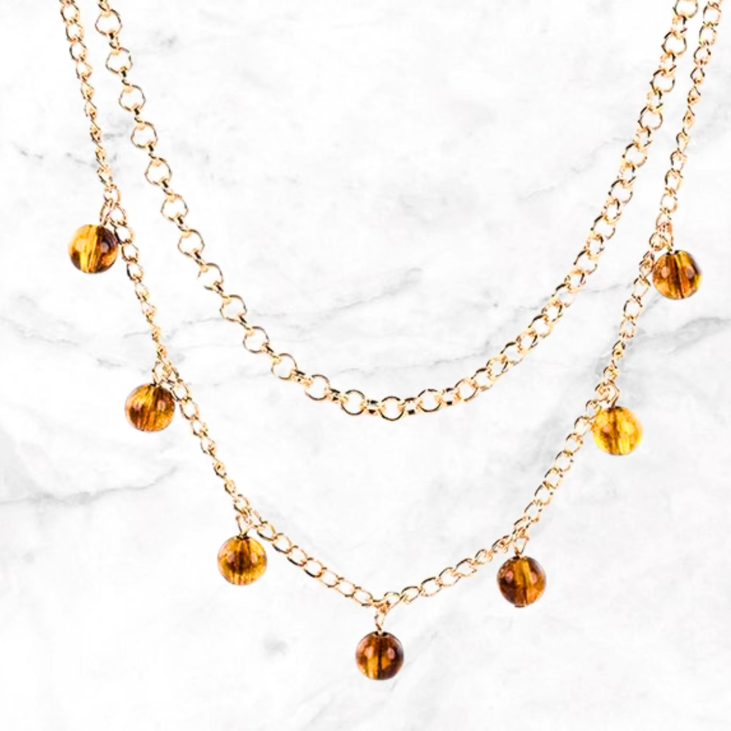 Close-up dubbele goudkleurige ketting met amberkleurige kristallen hangers