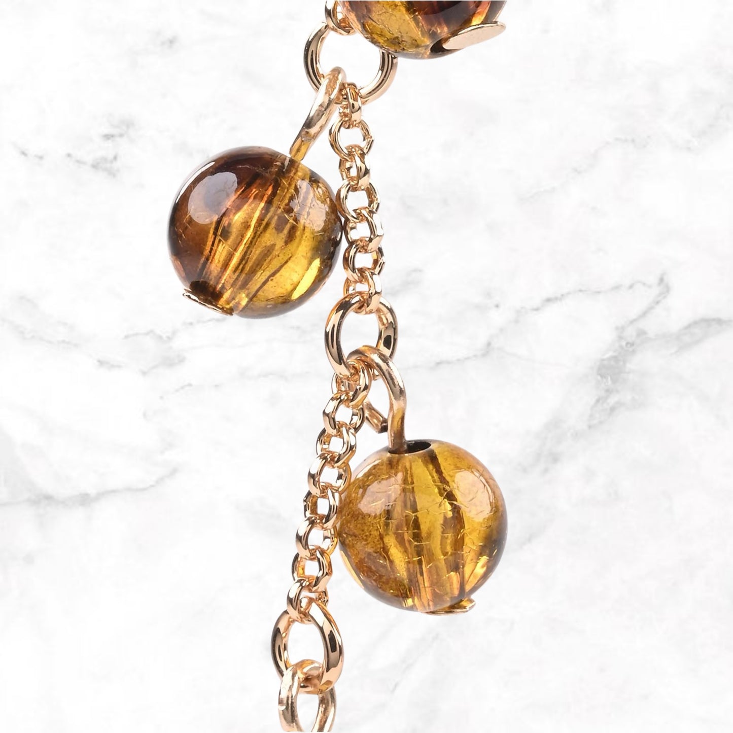 Close-up goudkleurig kettinkje met transparante amberbolkralen op marmeren ondergrond